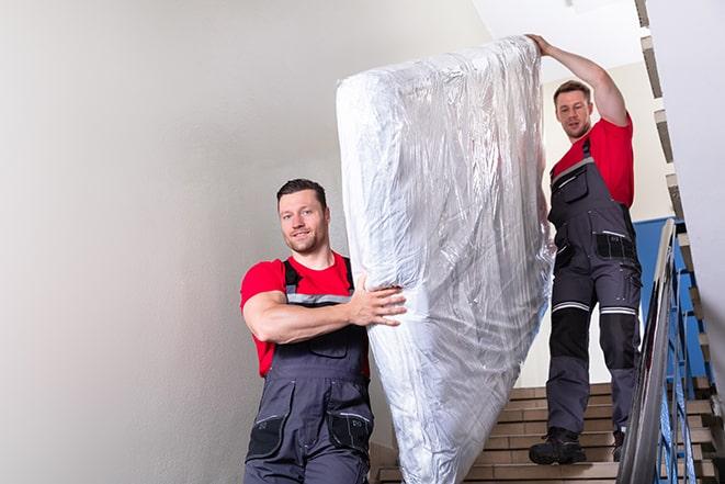 two people carrying a box spring out of a room in Hamtramck